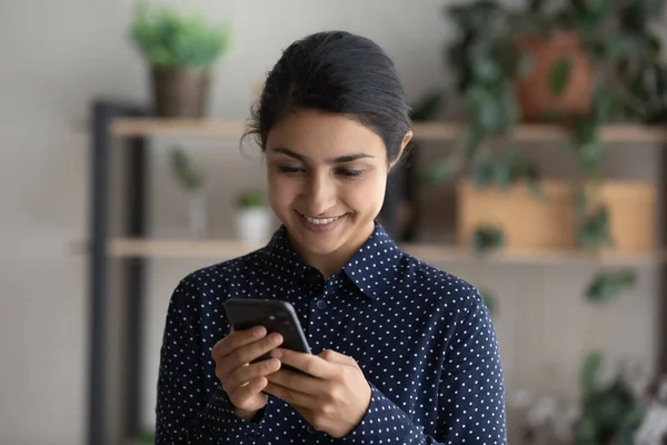 Happy Indian girl smiling at smartphone screen, holding mobile phone — стокове фото