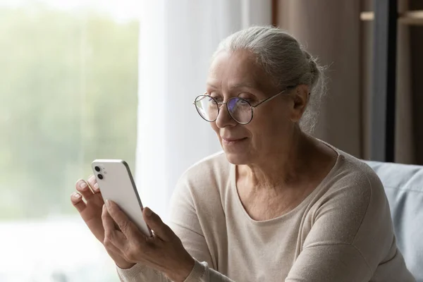 Happy middle aged woman in eyewear using smartphone. — стоковое фото