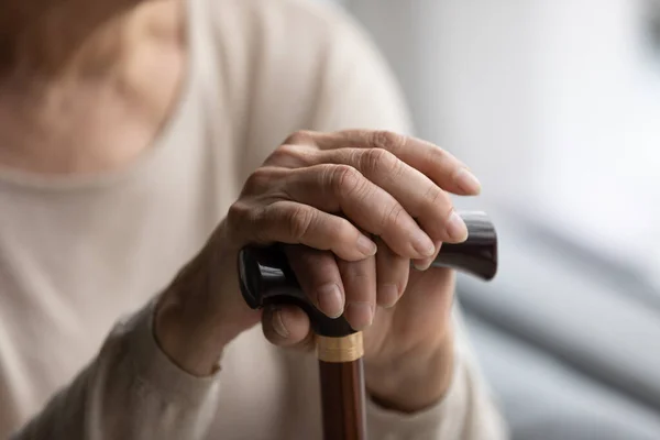 Close up focus on folded wrinkled female hands on wooden cane. — Fotografia de Stock