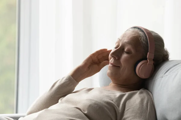 Relaxed middle aged woman listening music in headphones. — Stockfoto
