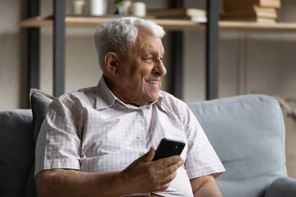 Dreamy smiling old man using cellphone at home. — стоковое фото