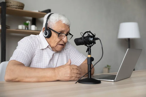 Focused mature retired man recording voice, vlogging at home. — стоковое фото