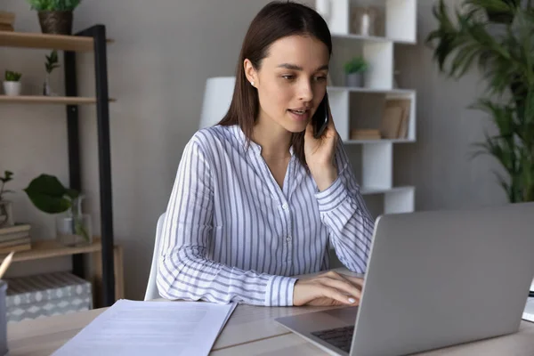 Seriös ung anställd talar i telefon och använder app laptop — Stockfoto