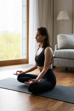 Huzurlu, güzel yogi kadın spor kıyafetleriyle evde meditasyon yapıyor.