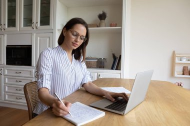 Bin yıllık gözlüklü öğrenci dizüstü bilgisayarına notlar yazıyor.