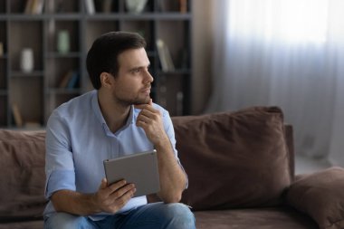 Düşünceli adam tableti tutuyor, çenesine dokunuyor, uzaktan bakıyor.