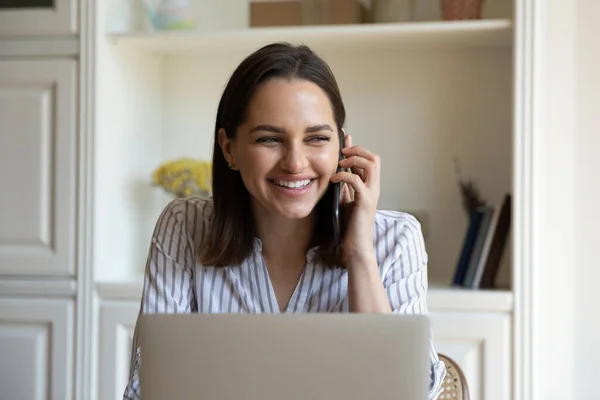 Щаслива дівчина користувача ноутбука розмовляє на смартфоні на робочому столі — стокове фото