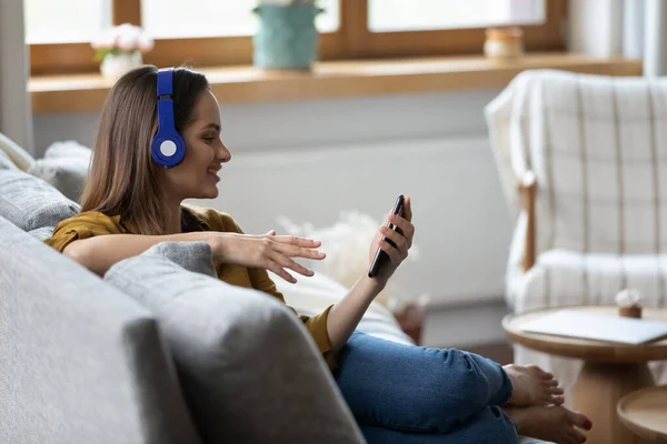 Happy pretty girl in headphones listening to music from smartphone — Stockfoto