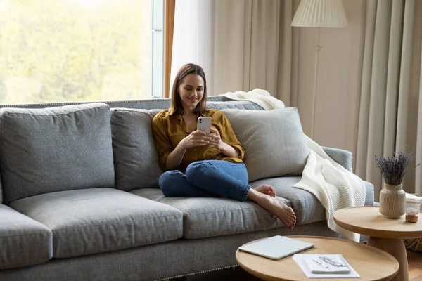 Happy millennial woman relaxing on couch at home — Stockfoto