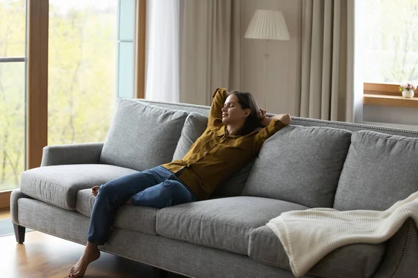 Rauhallinen tyttö venyttely kehon pehmeällä sohvalla olohuoneessa — kuvapankkivalokuva