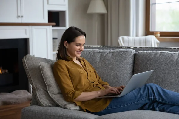 Cheerful happy millennial girl working at computer from home sofa — Stock Photo, Image