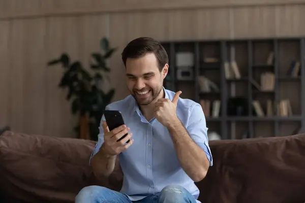 Homem animado olhando para a tela do telefone, mostrando o polegar até gesto — Fotografia de Stock