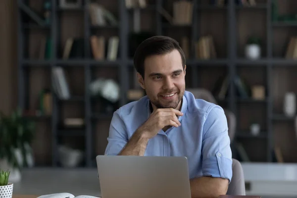 Усміхнений мрійливий бізнесмен, дивлячись на відстань, сидить за робочим столом — стокове фото