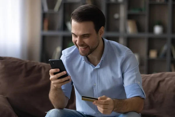 Emocionado hombre que paga con tarjeta de crédito de oro en línea, utilizando el teléfono inteligente — Foto de Stock