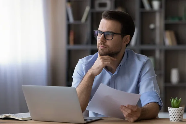 Thoughtful serious businessman in glasses touching chin, holding document — Stock Photo, Image
