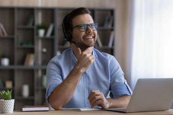 Hombre risueño con auriculares y gafas usando laptop, tomando notas —  Fotos de Stock