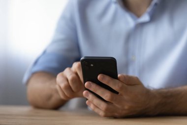 Kırbaç yakın adam akıllı telefon tutuyor, masada oturuyor.