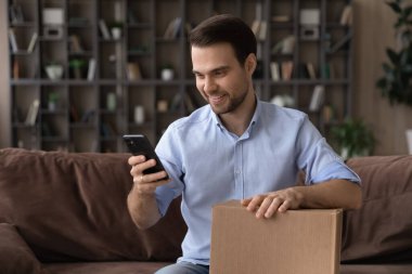 Akıllı telefon kullanan, karton kutu tutan, paketleri açan gülümseyen adam.