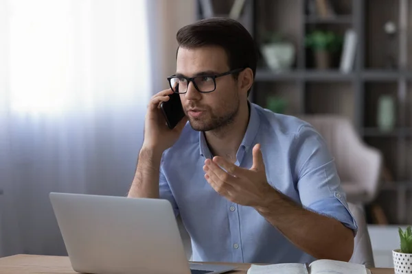 Впевнений бізнесмен в окулярах розмовляє по телефону, сидячи за столом — стокове фото