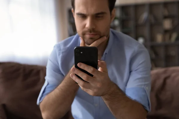 Close up homem pensativo olhando para a tela do smartphone, tocando queixo — Fotografia de Stock