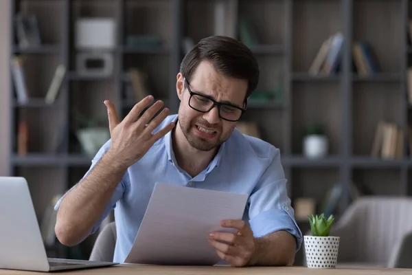 Unhappy frustrated man in glasses reading bad news in letter — стоковое фото