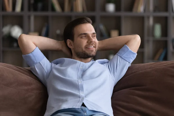Hymyilevä unenomainen mies rentouttava, venyttely sohvalla kotona — kuvapankkivalokuva