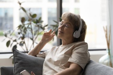 Kulaklıkla müzik dinleyen huzur içinde gülümseyen yaşlı kadın..