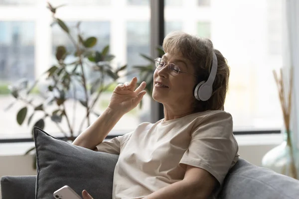 Smiling peaceful old retired woman listening music in headphones. — стоковое фото