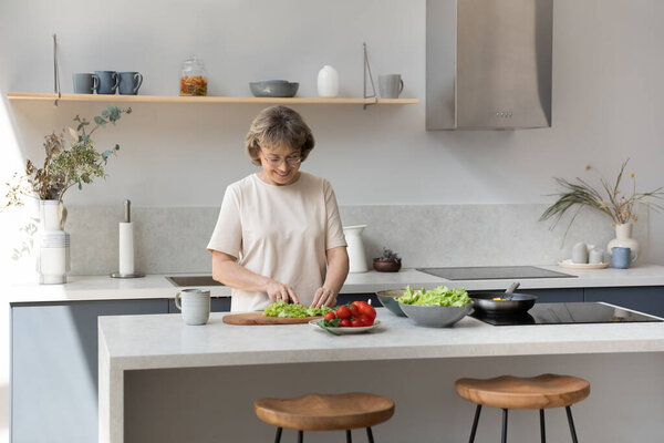 Happy old retired woman cooking in modern kitchen.