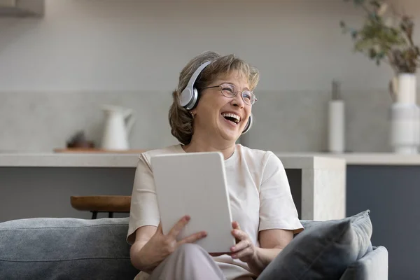 Happy elderly woman in headphones using digital touchpad gadget. — стоковое фото