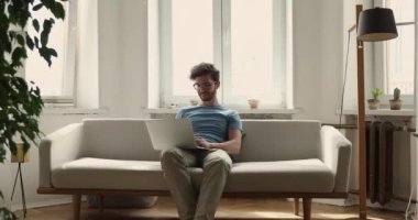 Millennial guy sit on sofa working on laptop at home