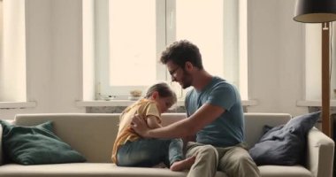 Young dad tickling his little cute daughter sit on sofa