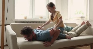 Little girl sits on daddy back playing together at home