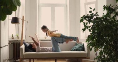 Mom lying on sofa raise on hands her little daughter