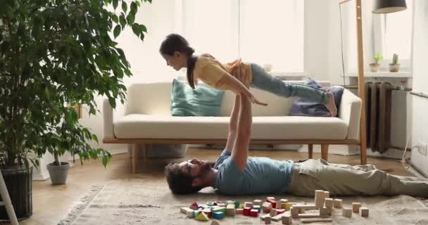 Dad lying on floor raise on hands his little daughter — ストック動画