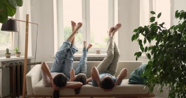 Couple and daughter lying on sofa fooling raising their feet — Stock video