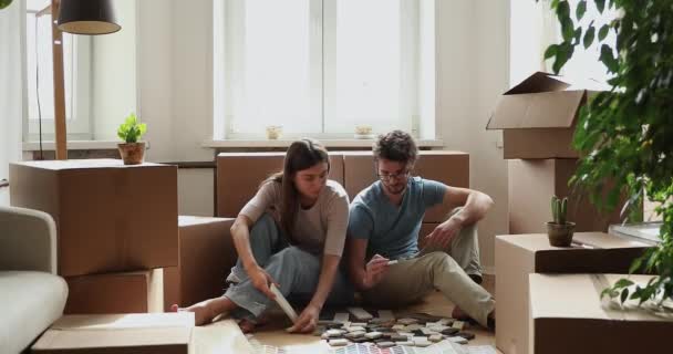 Couple sit near cardboard boxes choose tile swatches color — стоковое видео