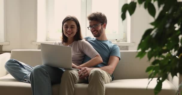 ミレニアル世代のカップルはラップトップを使用してオンラインで購入するソファでリラックス — ストック動画