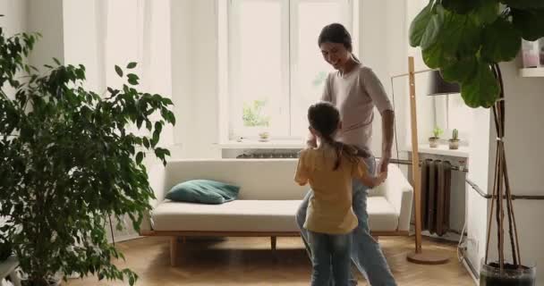 Mother and daughter holding hands swirling dancing in living room — Stock video