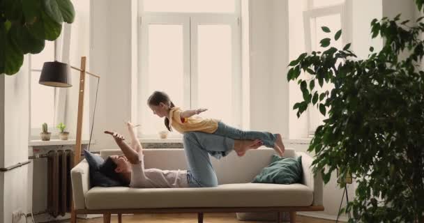 Mom lying on sofa raise on hands her little daughter — Stock video