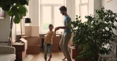 Happy father and daughter dancing in living room near boxes