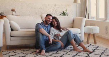 Happy homeowner couple sit on floor smile look at camera
