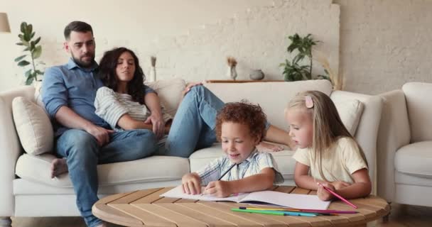 Preschool diverse children drawing with pencils, parents relaxing on sofa — Αρχείο Βίντεο