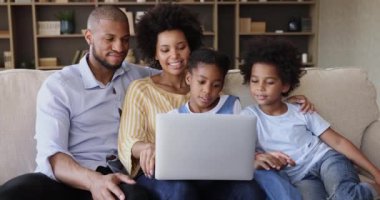 Black parents with kids watch video on laptop on sofa