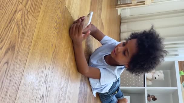 Little African boy lie on floor play game on smartphone — Stock video