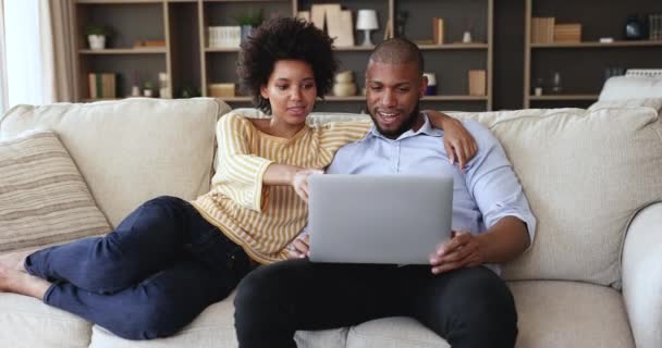 Happy Black couple rest on cozy couch talk use laptop — 비디오