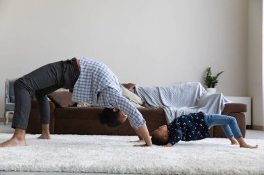 Active Black dad teaching preschool daughter to hold bridge stand
