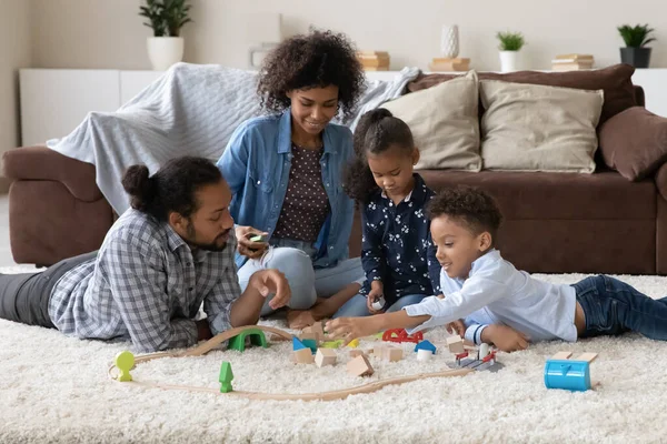 Happy parents helping two kids to build toy road model — 图库照片