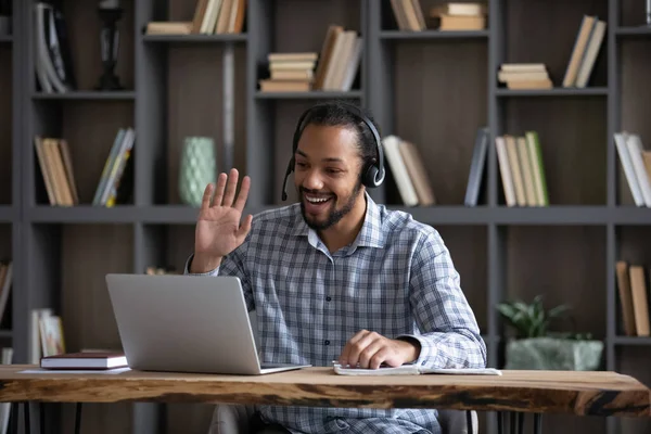 Friendly African guy in headphones with mic waving hand hello — Stock Photo, Image