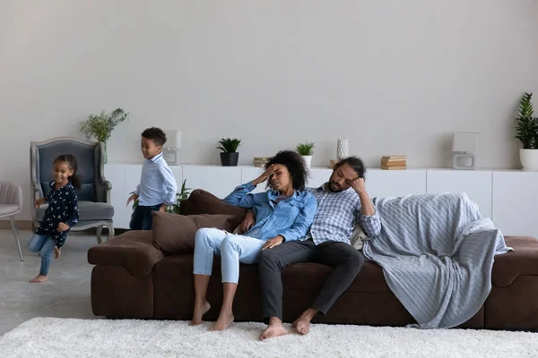 Tired African parents watching running naughty noisy kids — Stockfoto